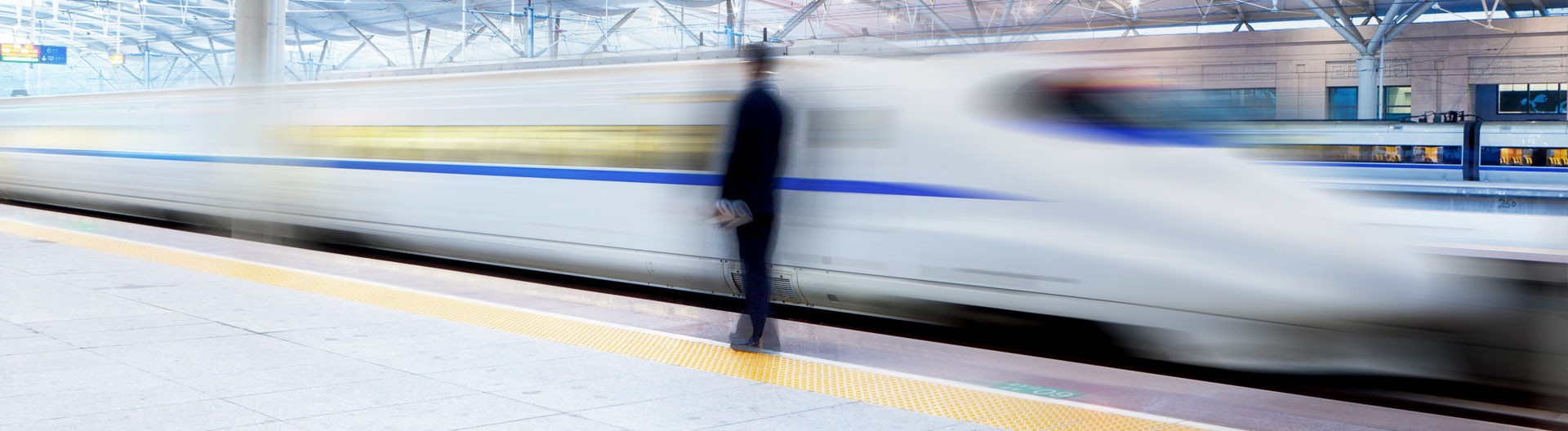 White fast train driving past a passenger at a train station