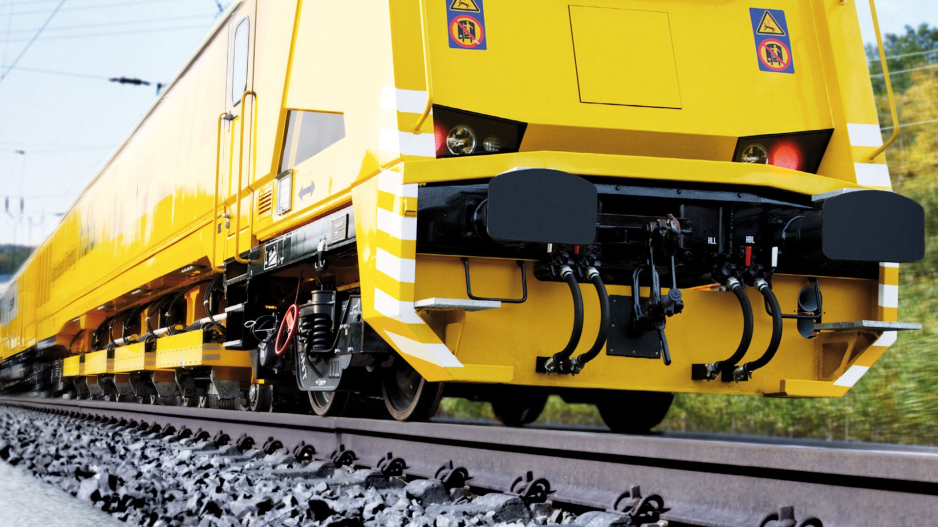 Yellow railway maintenance vehicle moving on tracks.