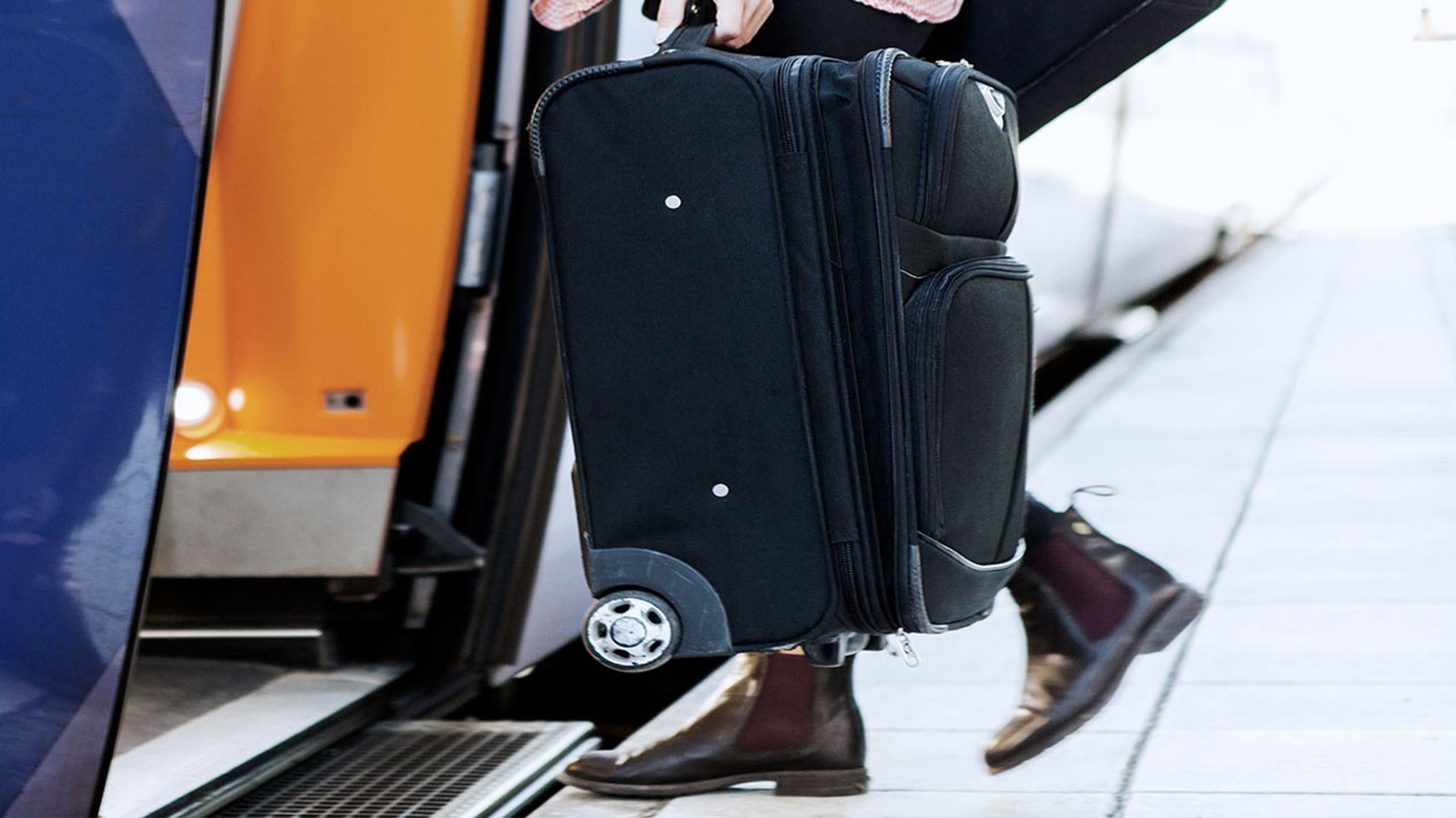 Person boarding train with rolling suitcase.