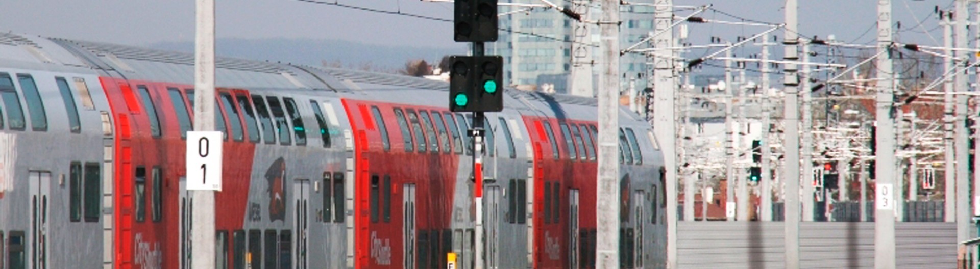 Double-decker train passing green signal lights.